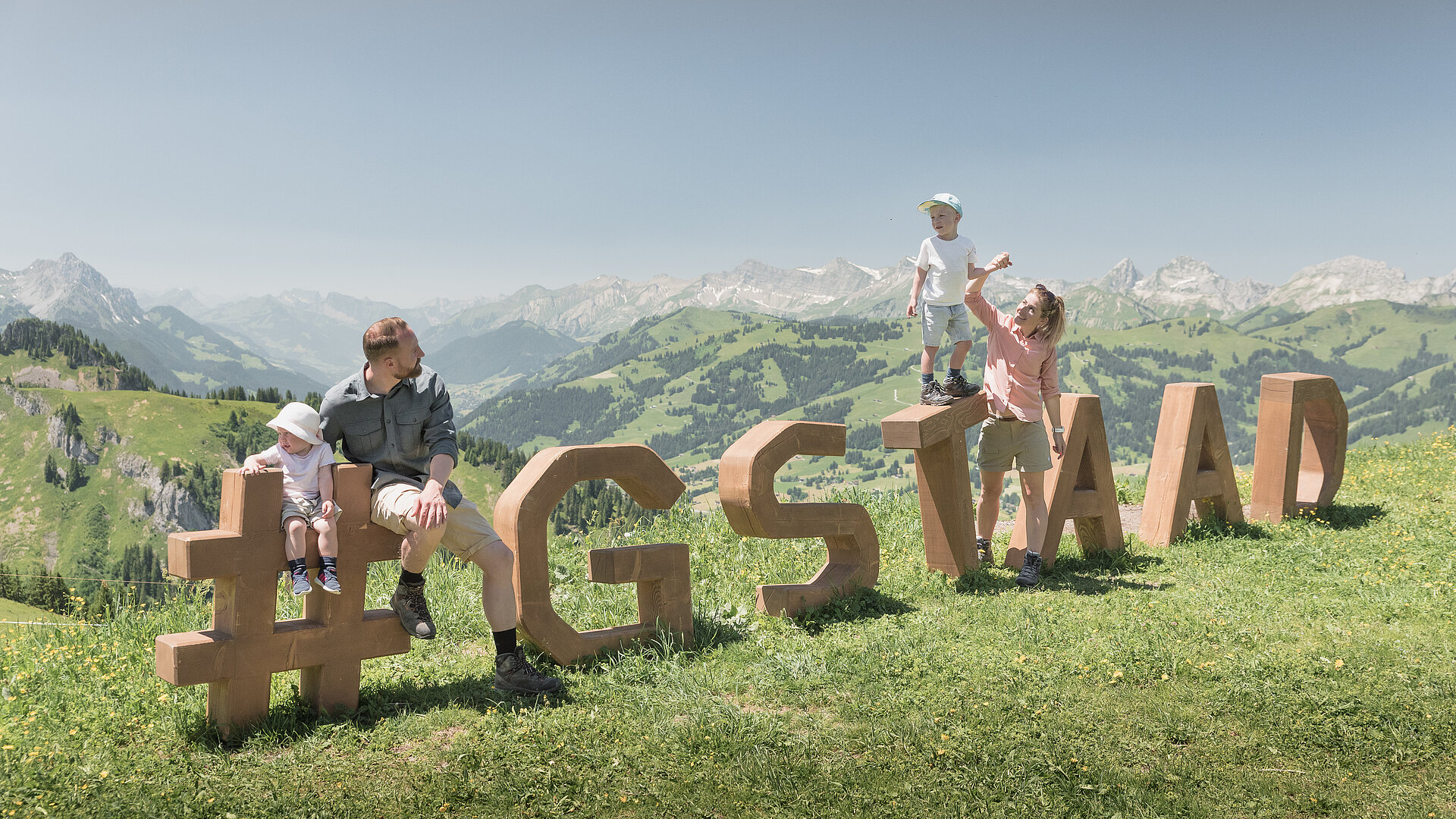<p>Eine vierköpfige Familie steht und sitzt auf dem Holz-Logo «Gstaad» Rinderberg im Sommer.</p>